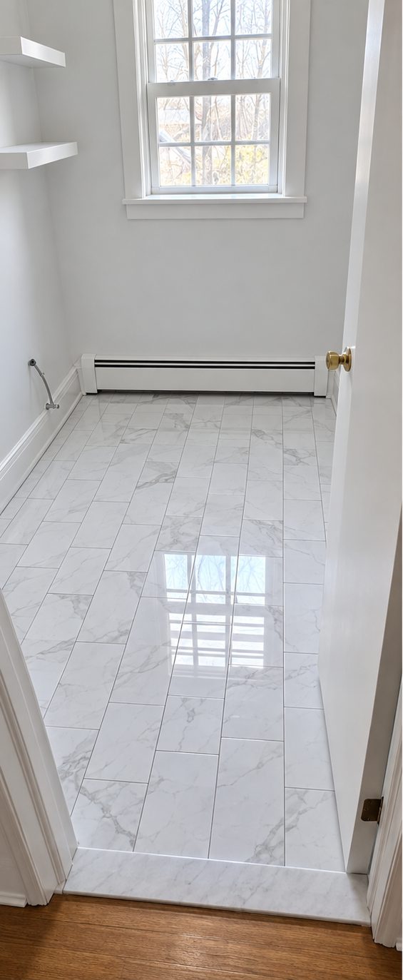 Finished bathroom floor in large white veined tile with a marble threshold